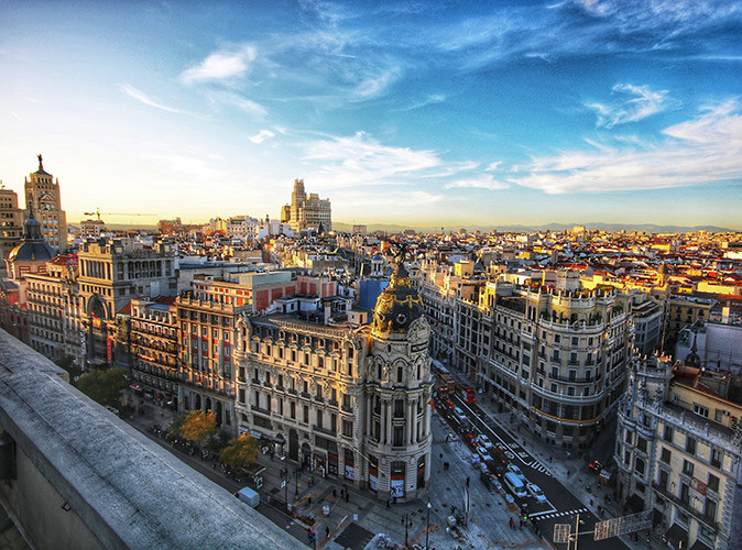 Moving to Madrid Aerial view of a city skyline showing historic gray and beige buildings, streets with cars and pedestrians and a blue sky with some clouds