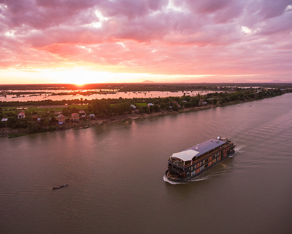 A long, narrow, small ship cruise on the mekong river wuring sunset