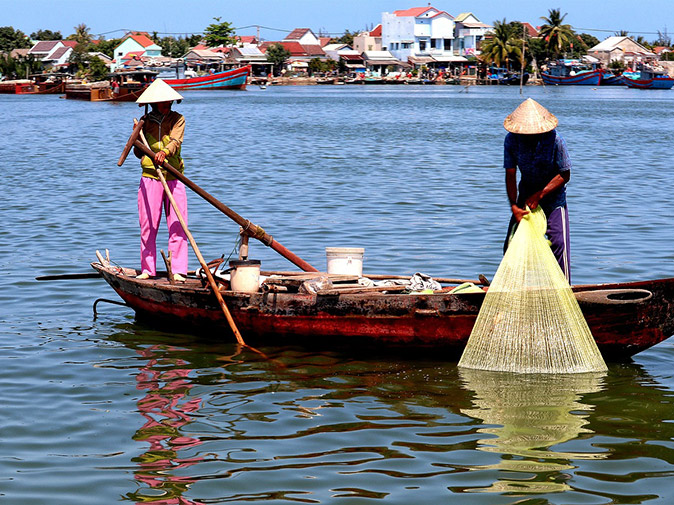 Experiencing local life on a Mekong River cruise 2 people with traditional Vietnamese hats in a small wooden boat, one holding a fishing net