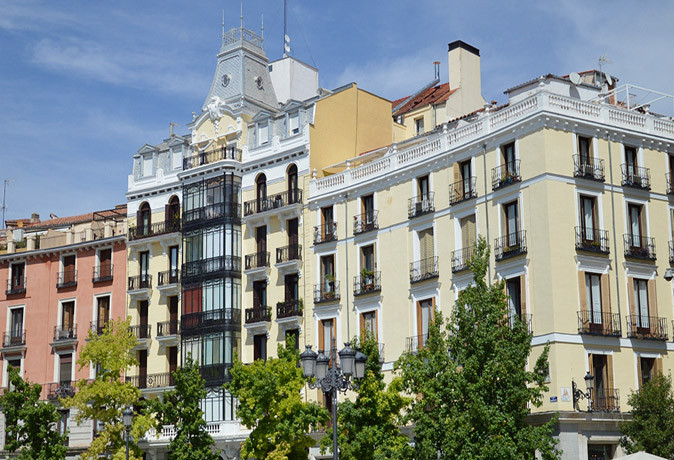 Things to know about housing in Madrid An apartment block with white and pink exterior, with small Spanish style balconies and a few trees at the bottom