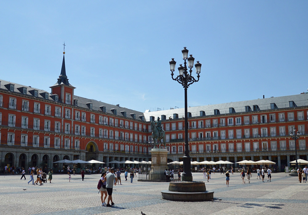 A large city square with several people, surrounded by red, Spanish buildings