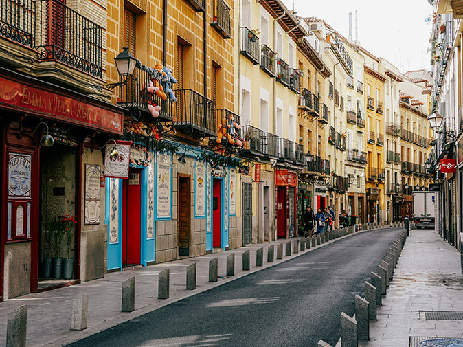 Things to know about the cost of living in Madrid A spanish street with a restaurant in the foreground and gray and beige buildings lining the street