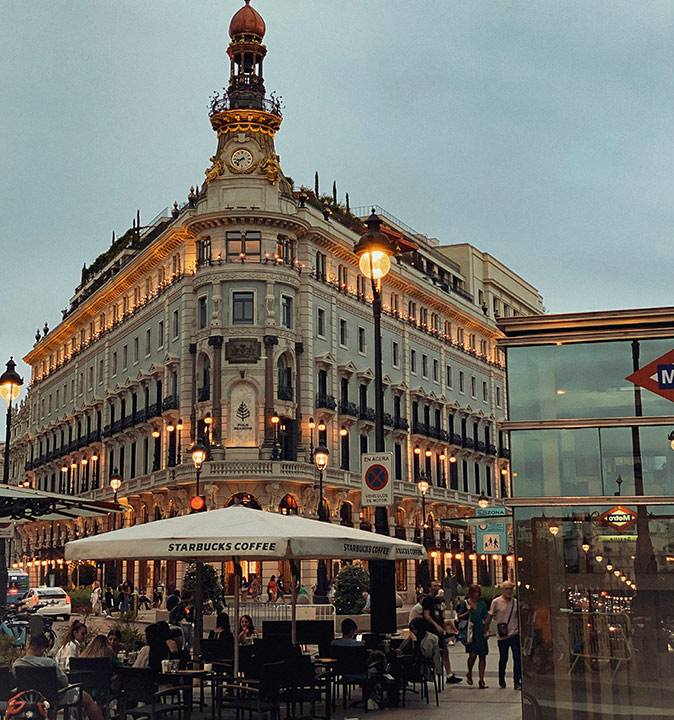 Tips for building a social life in Madrid A busy terrace in a city after sunset showing part of a historic building and part of a modern metro entrance