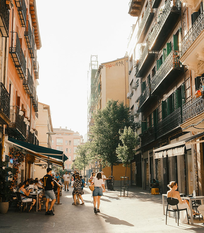 Tips for moving to Madrid A woman walking on the streets of Madrid, showing terraces with people on both sides and apartment buildings on both sides
