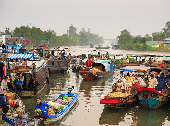 A floating market on the Mekong River in Vietnam Several small wooden boats with people selling fruits and vegetables on a brown river with some greenery in the background