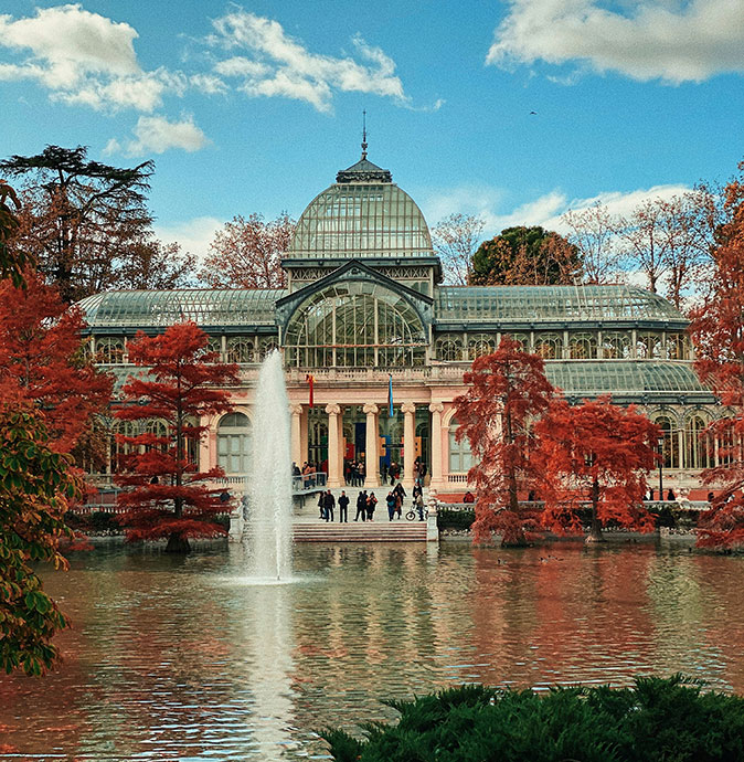 Things to know about the weather in Madrid A large pond with a fountain, trees in fall colors and a historic building in gray and pink shades