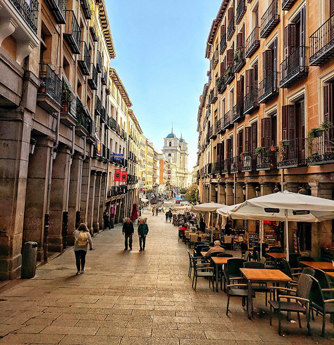 Life in the center of Madrid A typical street in the center of Madrid showing a cafe terrace, several people and historic looking apartment buildings on both sides
