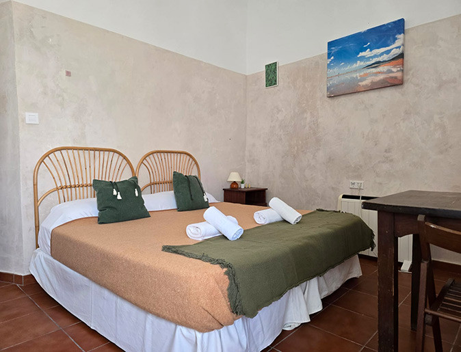 A coliving space in Tarifa, Spain A large double bed and part of a wooden desk in a room with white and beige walls