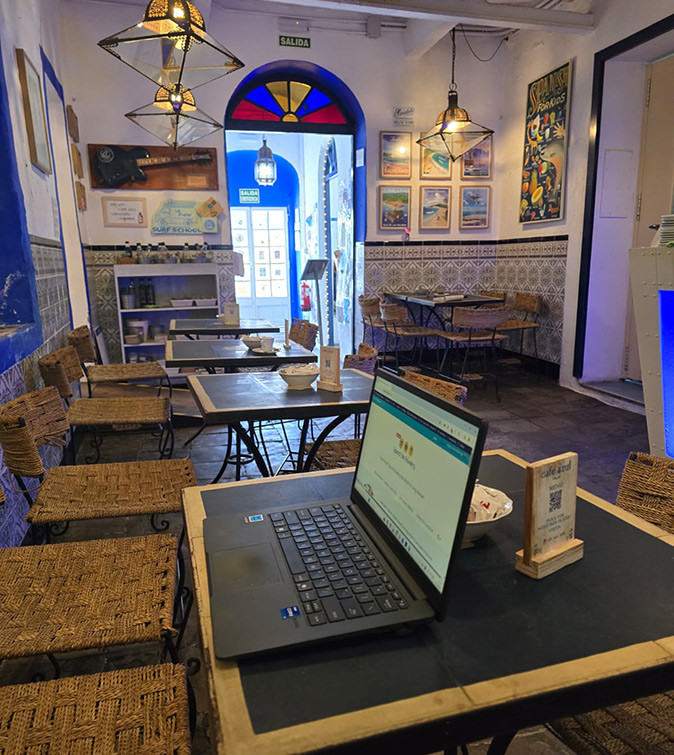 Working remotely from a cafe in Tarifa A laptop open on a table in a cafe showing several tables and chairs and a cozy atmosphere