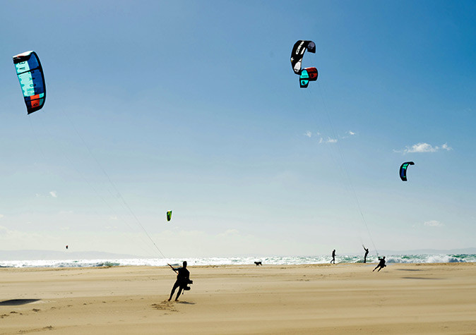 Kitesurfing in Tarifa Various kitesurfers on a sandy beach with waves in the background