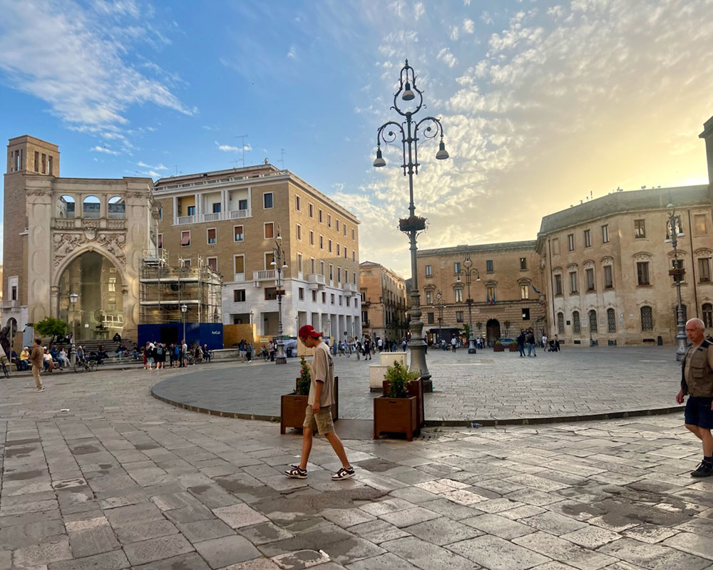 A typical Italian plaza with several people walking, surrounded by white and beige buildings