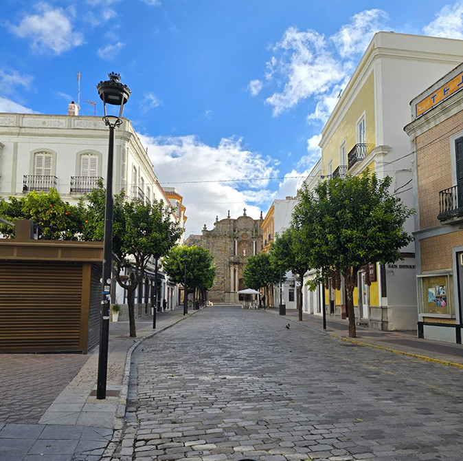 The historic center of Tarifa, Spain A cobbled street lined with trees and white, yellow and brown buildings