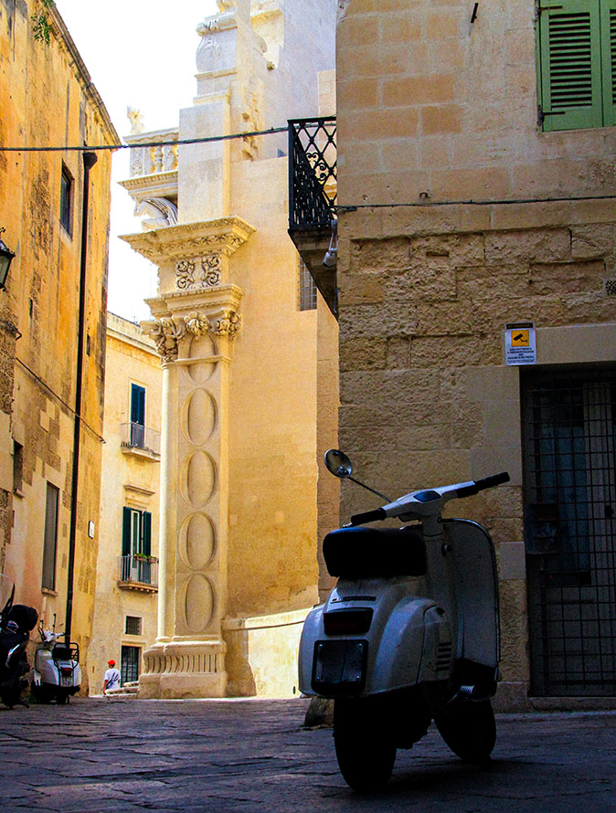 A narrow Italian street showing parts of brown and beige buildings, and a parked Italian scooter