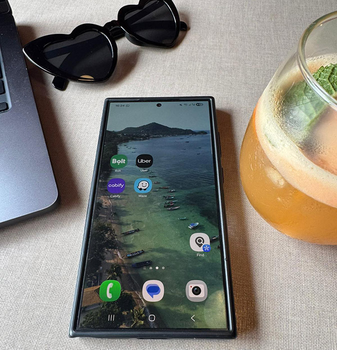 How to use your phone when traveling abroad A smartphone showing several apps, with part of a laptop, sunglasses and an orange drink in the background