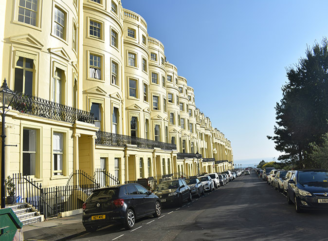 A row of houses paited light yellow, along a road with parked cars