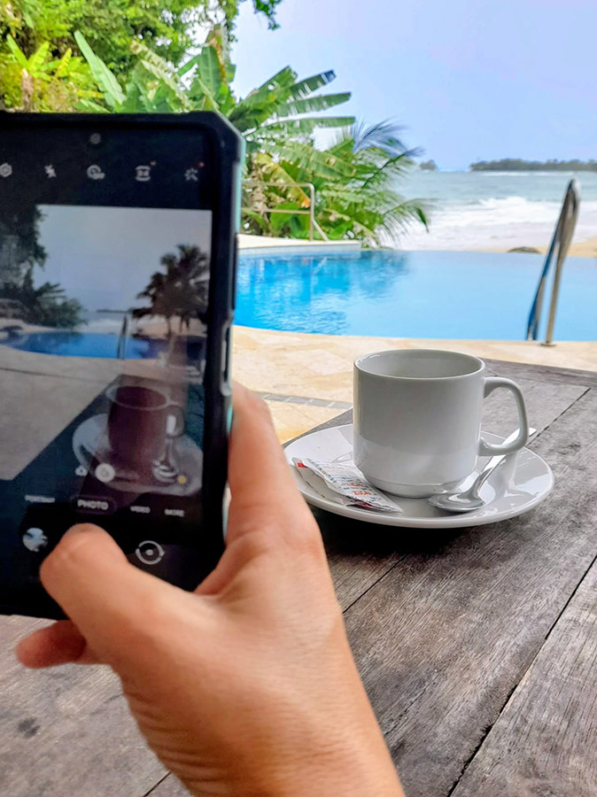 Staying connected abroad A hand holding a phone taking a picture of a coffee cup with a pool and beach in the background