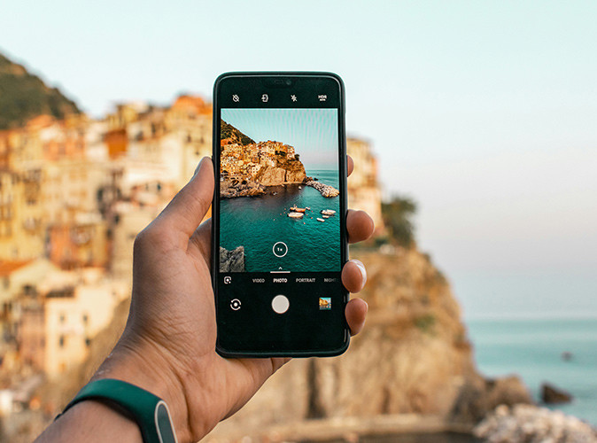 Tips for using your phone in Europe A hand holding a phone showing the Italian coastline which is also pictured out of focus in the background