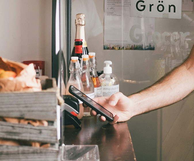 Tips for paying when traveling abroad A hand holding a phone paying contactless at a counter with some food items showing