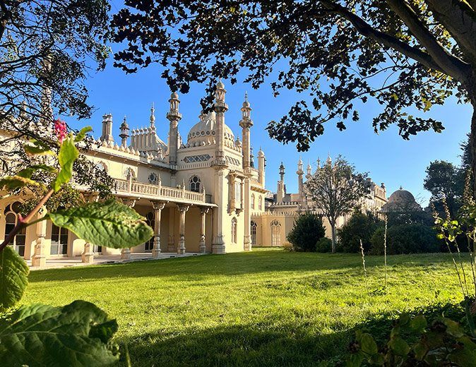 A beige historic building with grass and trees in front of it