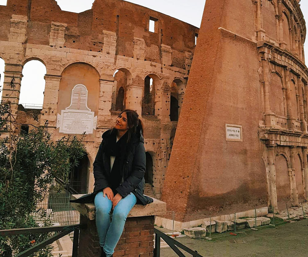 A woman smiling, sitting in front of Roman ruins