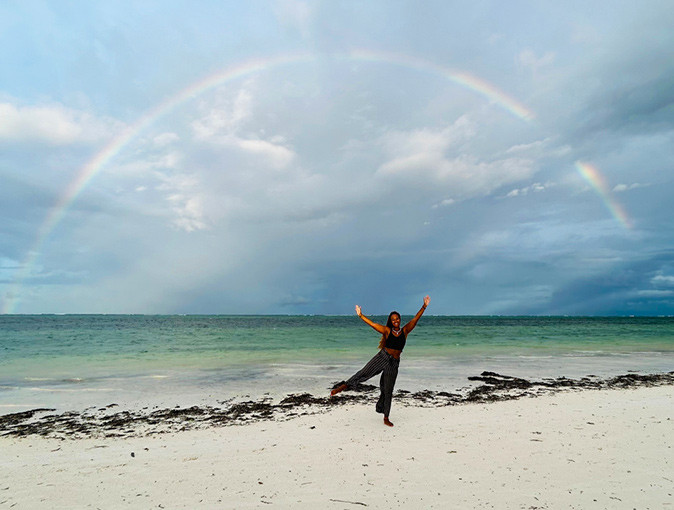 A digital nomad on a sandy beach with a full rainbow above her