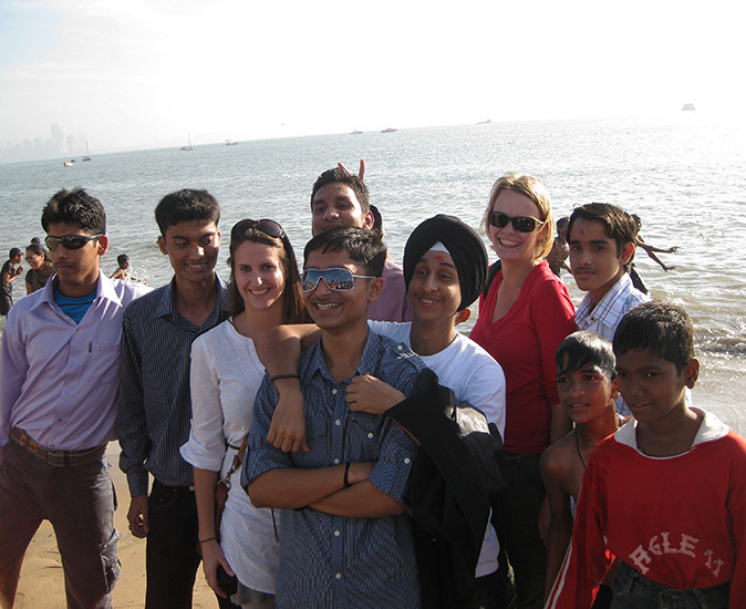 2 caucasian women in a group of young Indian men on a beach posing for a picture