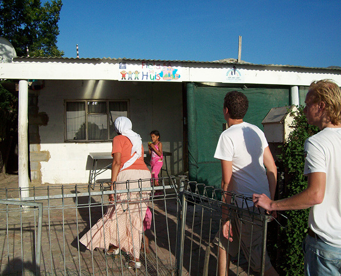 3 people walking towards a white community building with a child standing in front of it