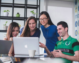 4 young adults looking at a laptop screen in a bright office setting