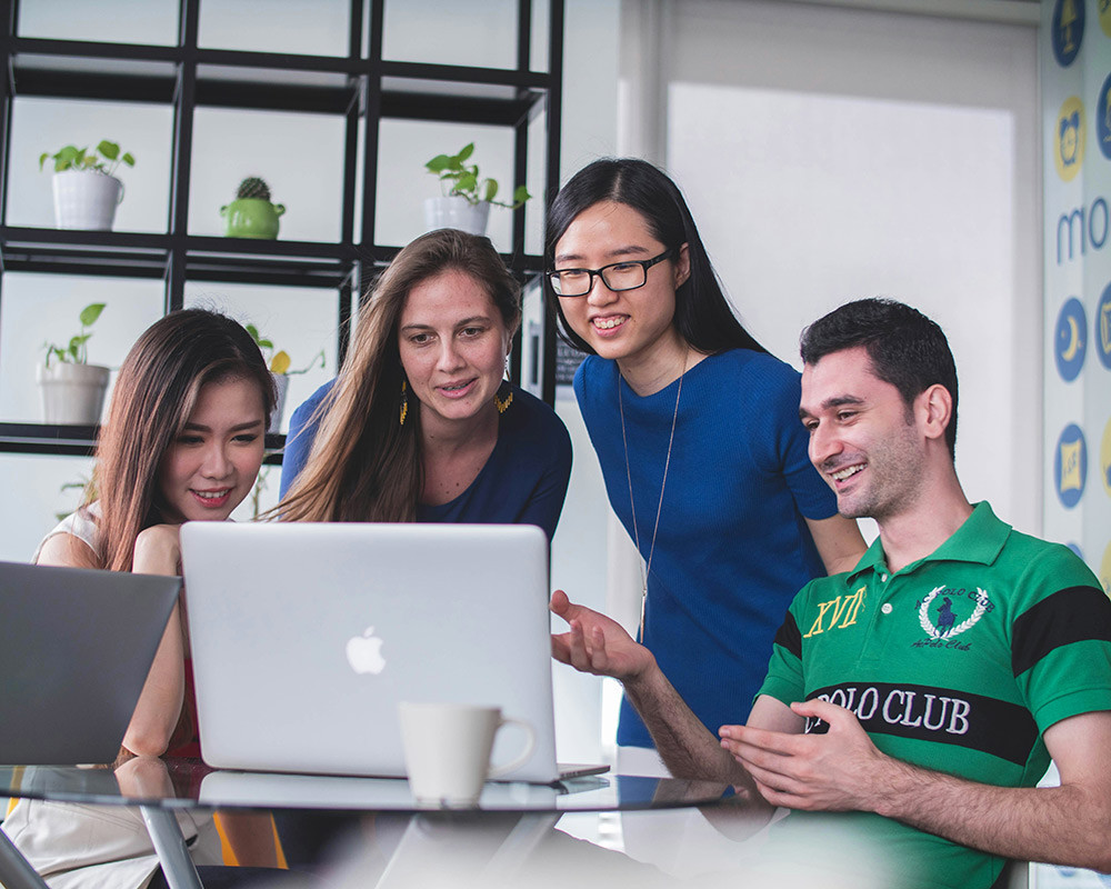 4 young adults looking at a laptop screen in a bright office setting