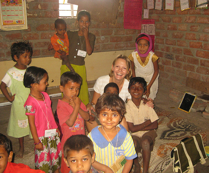 A young female teacher smiling surrounded by small kids in a simple classroom setting