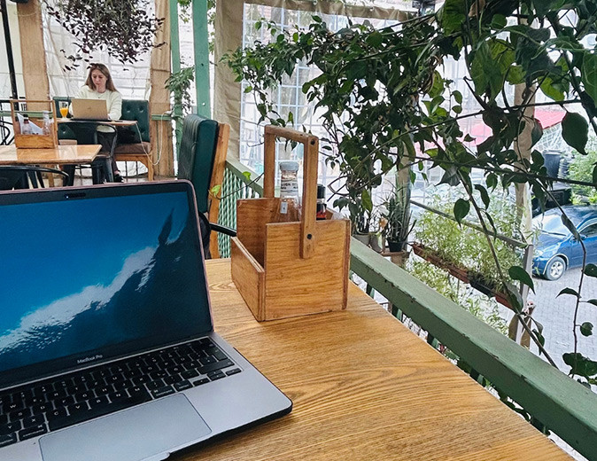 A laptop in a cafe with another woman working on her laptop in the background