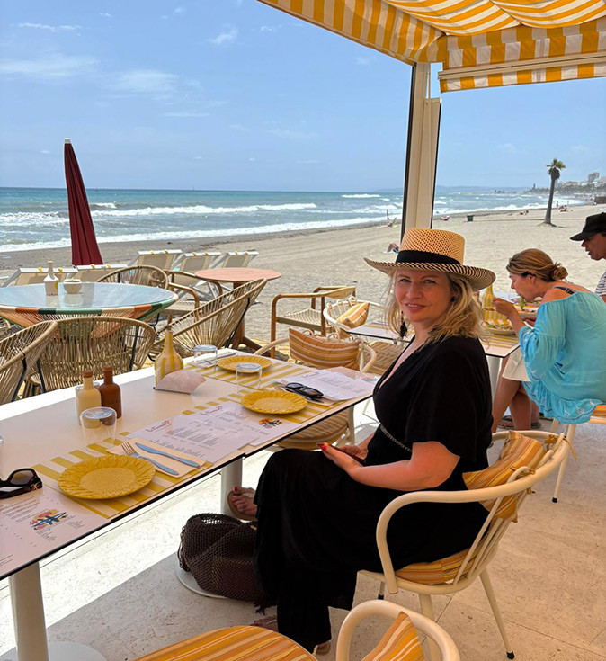 A woman smiling at the camera sitting in a beach bar in Estepona with the sea in the background