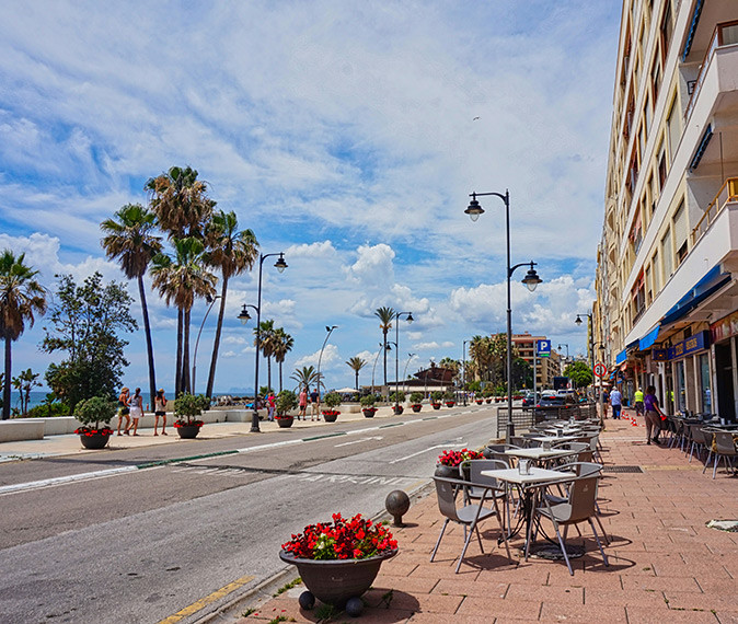 Coastal part of Estepona showing apartment buildings and terraces on the sidewalk on one side of the road, with palm trees and the sea on the other side