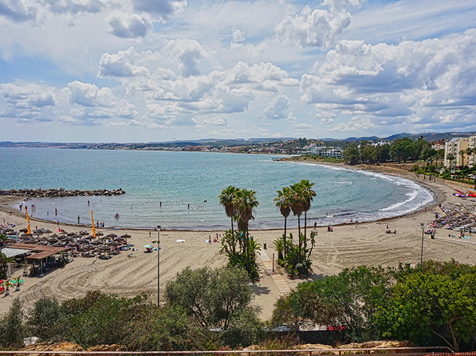 A bay in Estepona showing a sandy beach with sun loungers, palm trees and some buildings