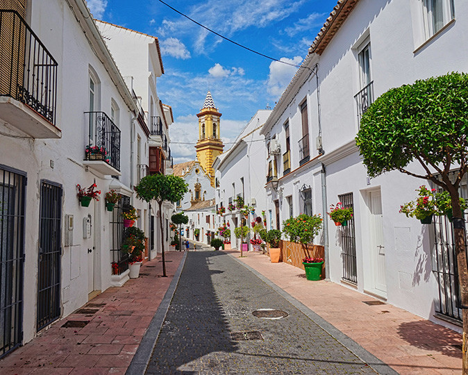 A narrow street with whitewashed houses on both sides and a church in the background