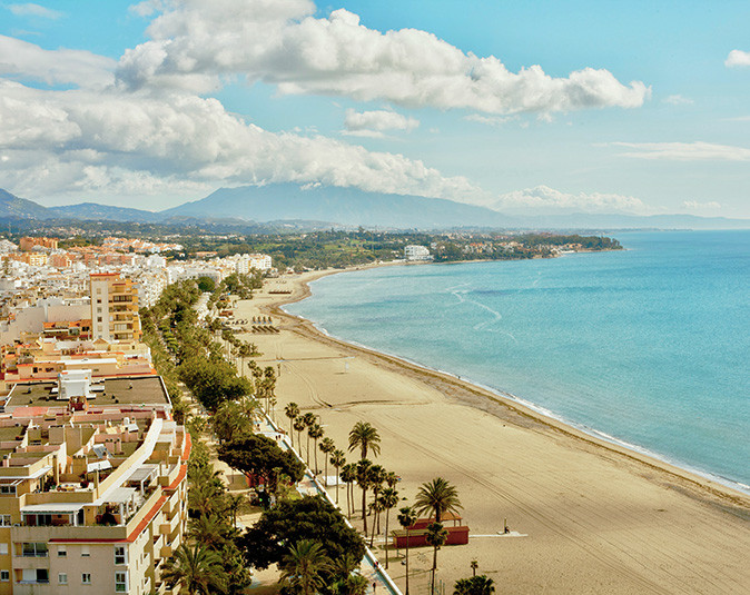 Aerial view of the coastal town of Estepona showing a long sandy beach lined with trees and buildings
