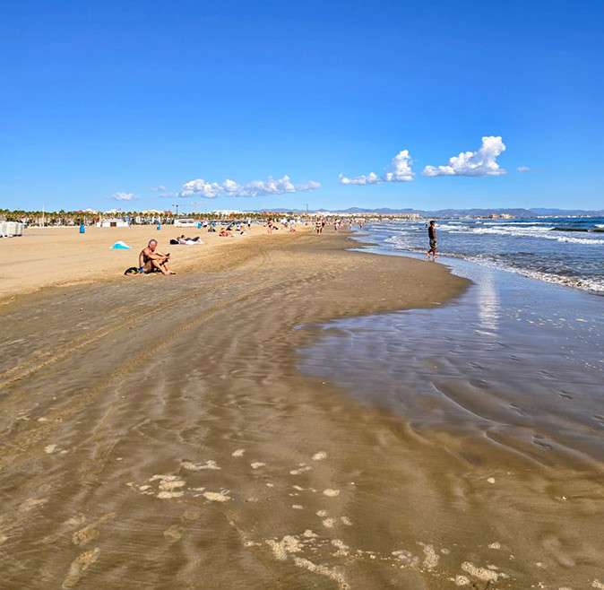Sunny weather in Valencia most of the year A long sandy beach with several people and a blue sky