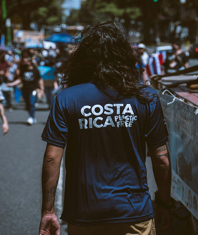 A man facing away from the camera wearing a blue shirt with the text "Costa Rica Plastic Free"