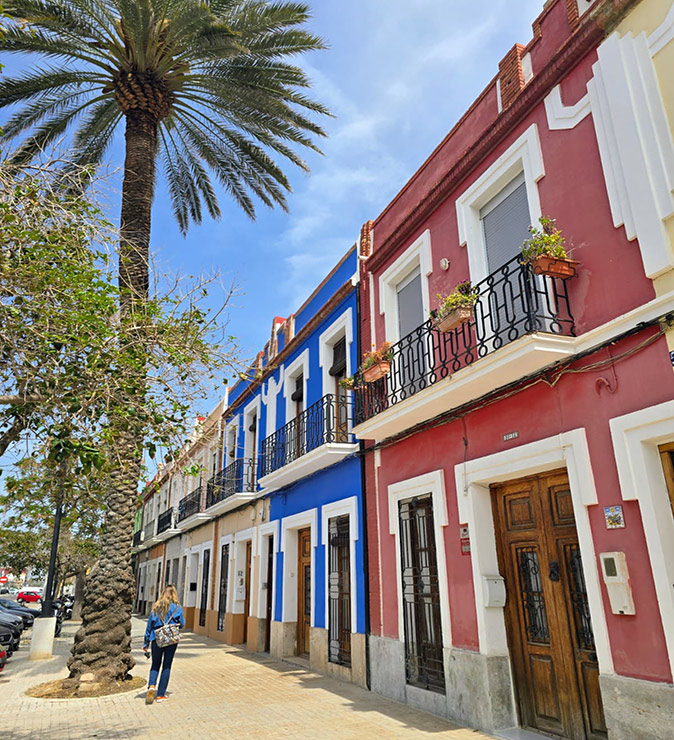 Housing costs in Valencia for digital nomads A row of colorful houses with a woman walking past and a palm tree in front of it