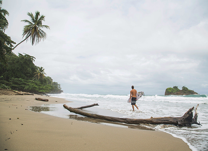 A man with a surf board on a sandy beach in Costa Rica