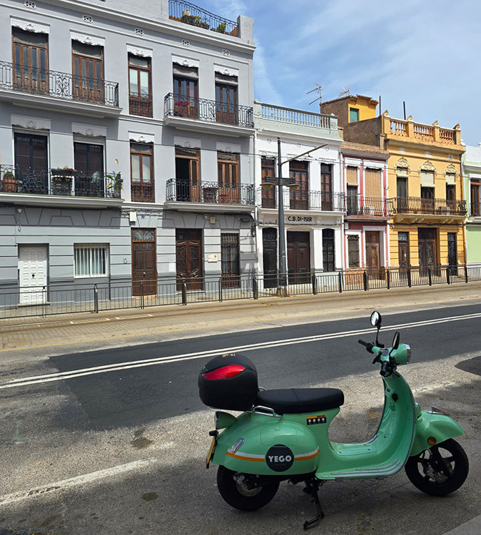 How to get around Valencia as a digital nomad A light green scooter parked in front of colorful historical houses