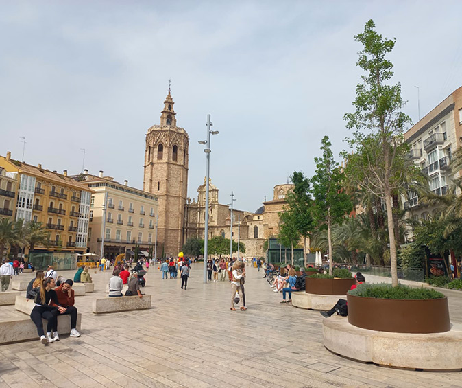 Valencia as a digital nomad destination A city square with several people walking and sitting, surrounded by some greenery and historic buildings