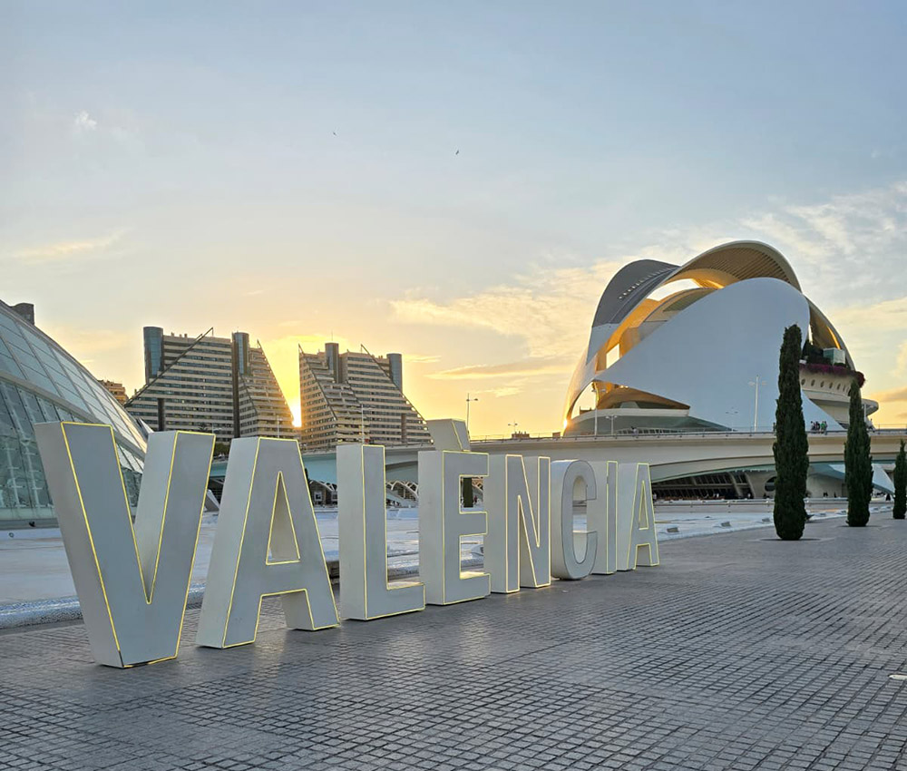 Giant white letters spelling Valencia places in front of the futuristic City of Arts and Sciences building in Valencia city