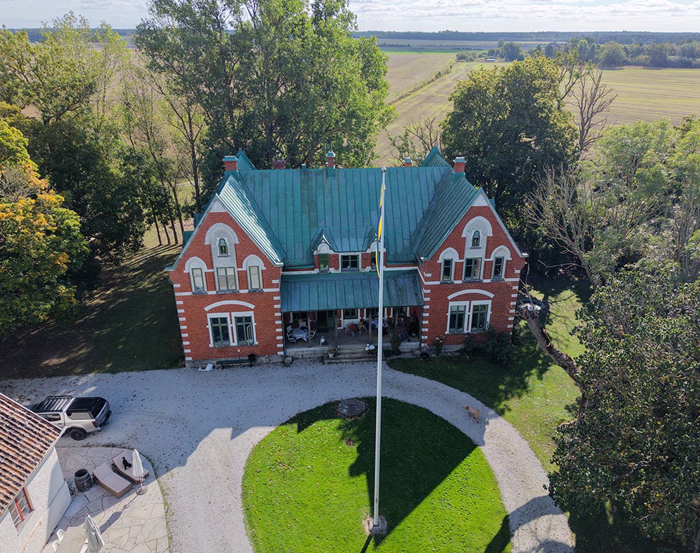 Drone shot of a historic red home with a green roof in a Swedish landscape on the island of Gotland