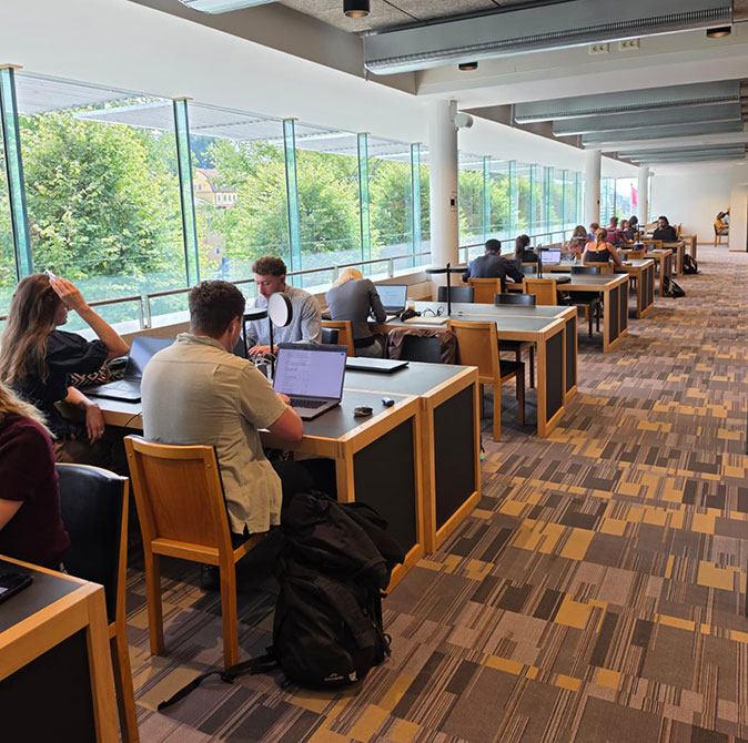 Working from a library during a coworking retreat rows of desks and chairs with several people, inside a brightly lit library