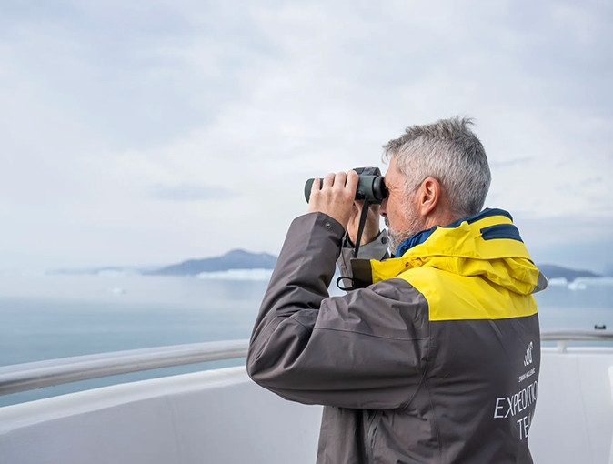 Experiencing a Ross Sea Expedition An Antarctic cruise scientist looking out to sea through binoculars