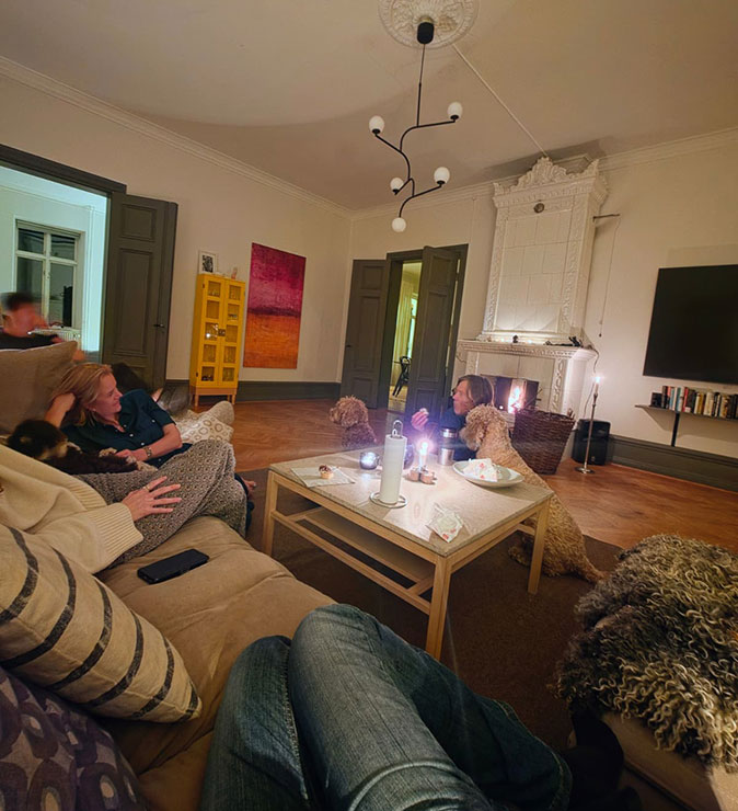 Community at a coliving in Sweden People sitting on and next to sofas in a dimly lit, cozy livingroom